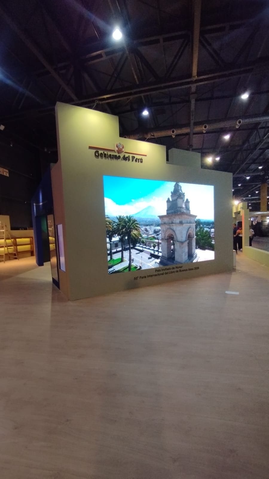 Painel LED horizontal integrado à frente de um estande, exibindo imagens de uma cidade.