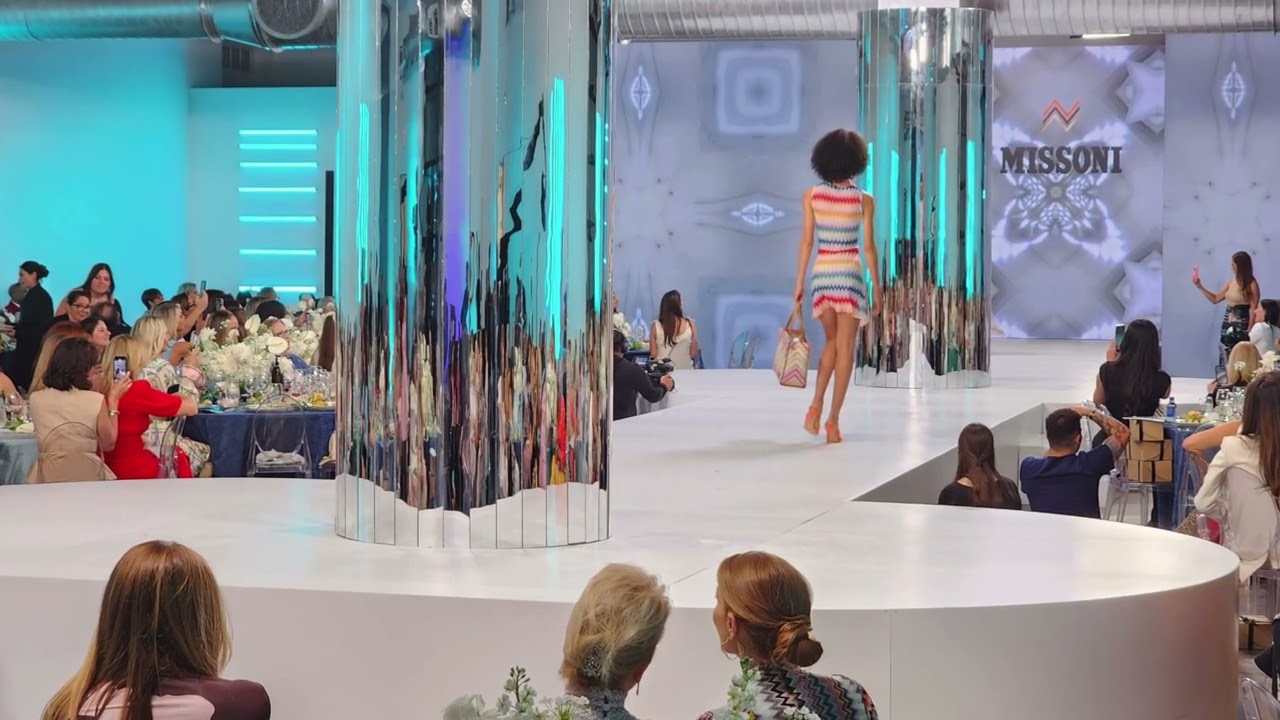 Podium blanc incurvé autour de colonnes miroir, avec écrans LED droits en fond de scène.